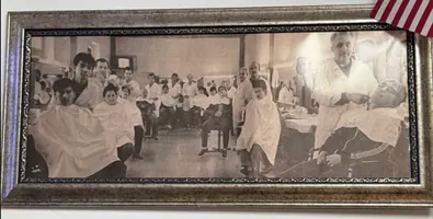 A black and white photograph of a busy barbershop with a row of barbers at work